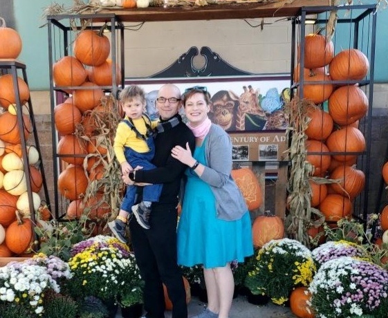 Mom, dad, and young son dressed up as characters from movie Despicable Me Standing in front of a pumpkin arch.  