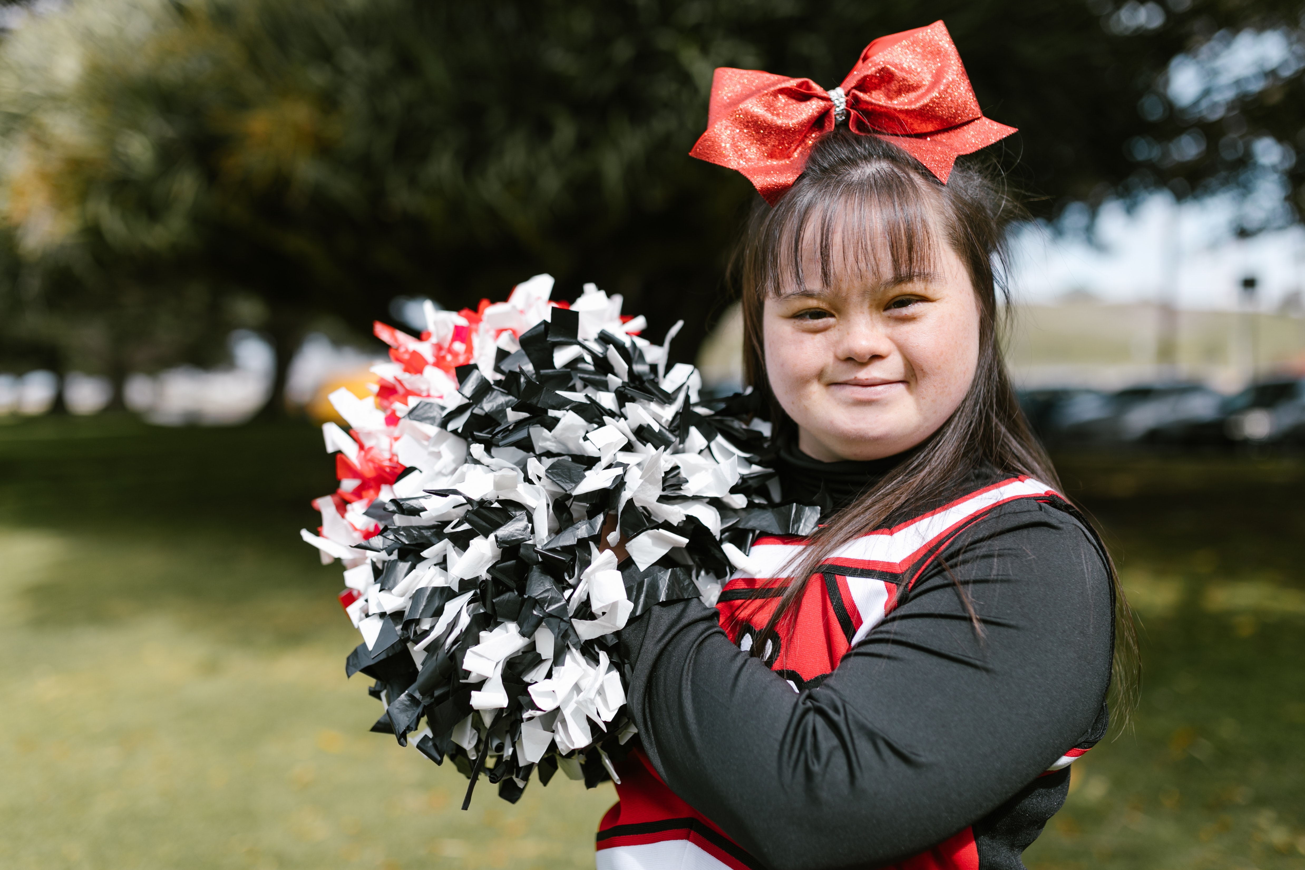 A young girl with Down Syndrome wears a black, white, and red cheerleading outfit.